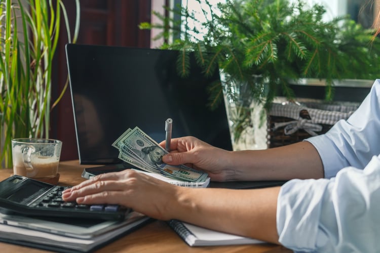 Person using a calculator at their desk with money in their hand