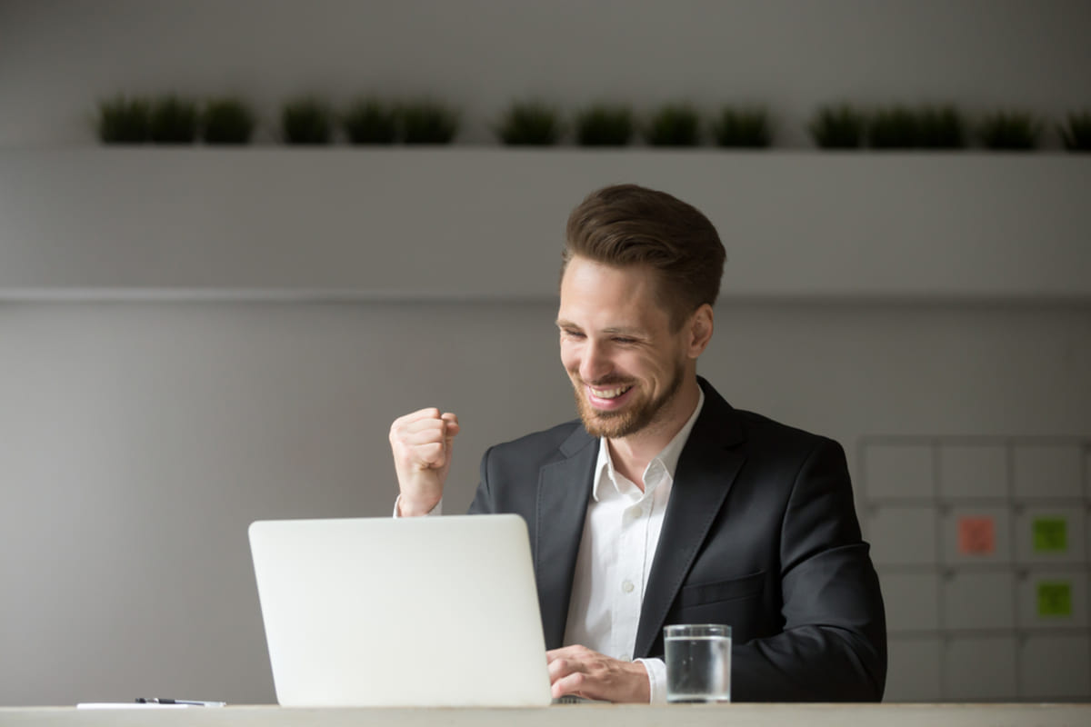 A happy man sitting at his laptop celebrating