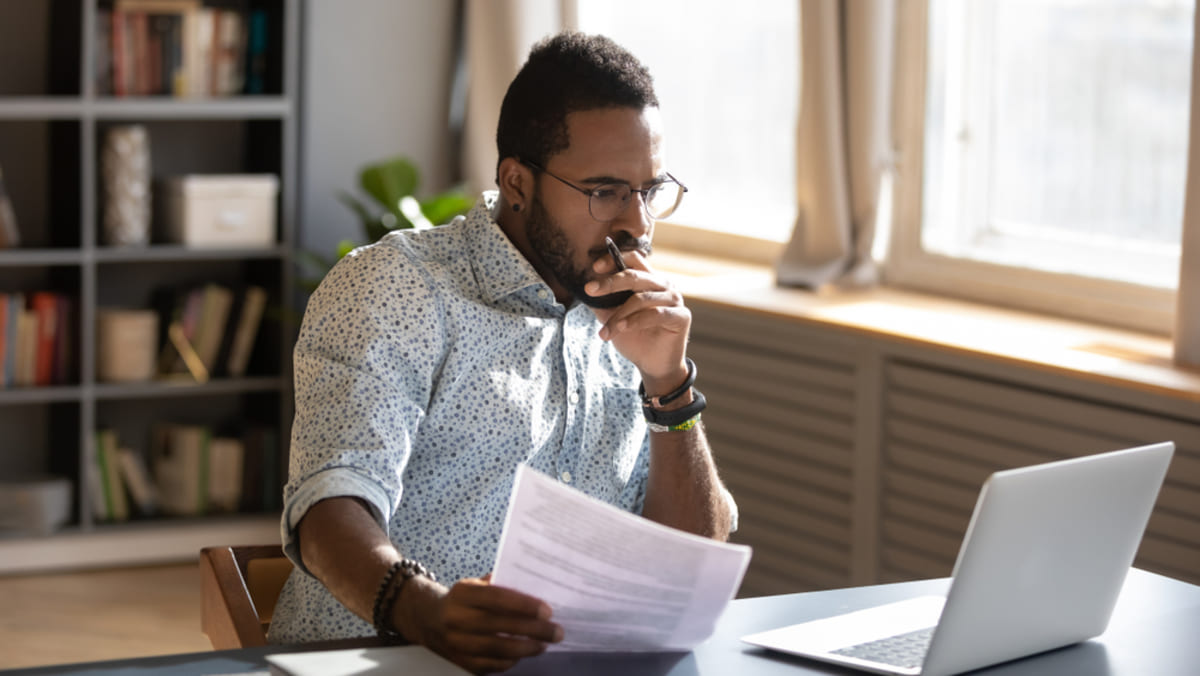 A man conducting research on a laptop and holding documents