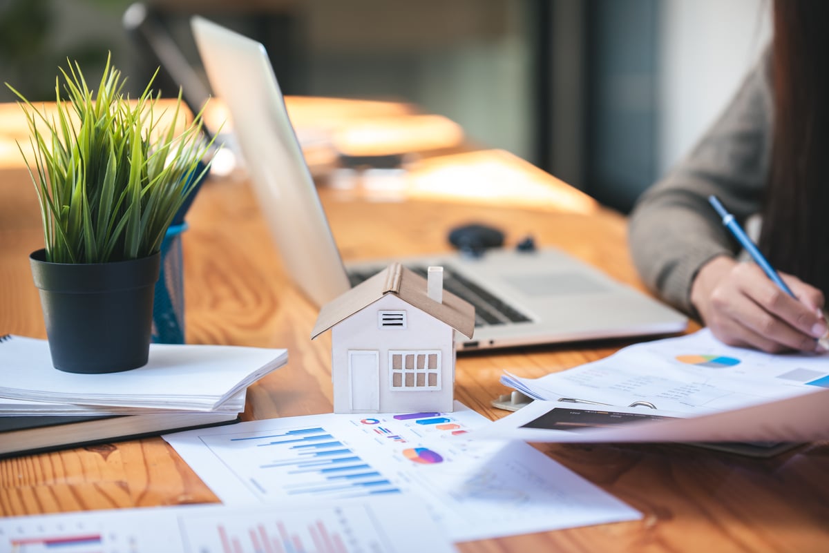 A small house next to papers with graphs and charts on them