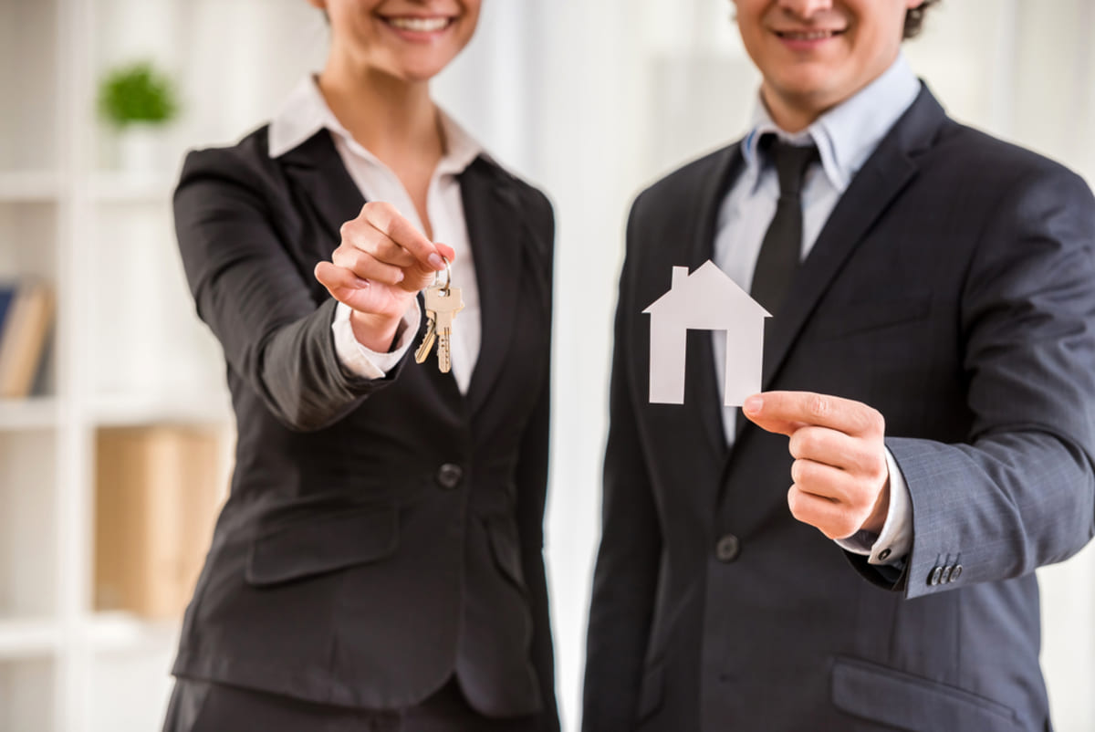 A woman holding keys next to a man holding a house