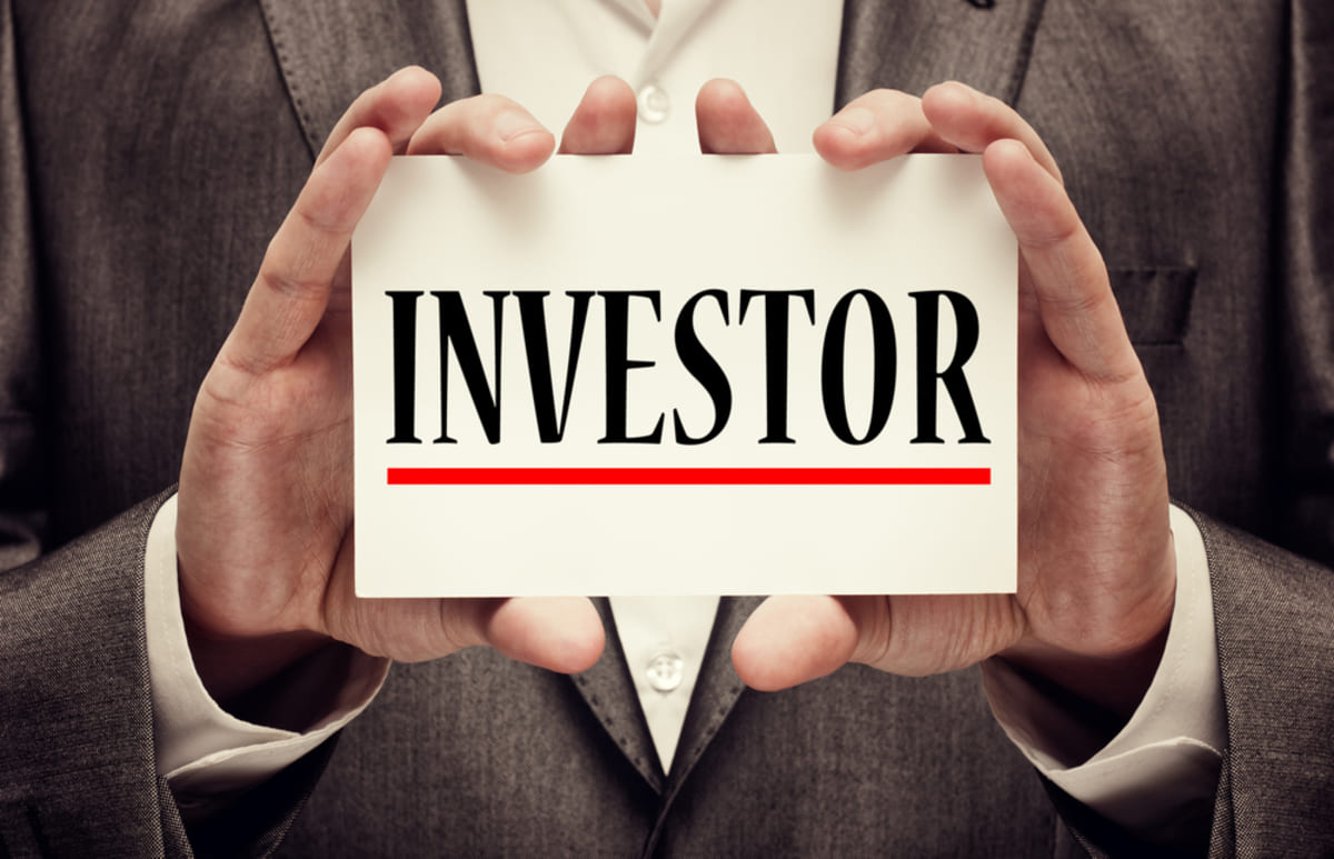 Hands holding a card with Investor on it, passive real estate investing concept