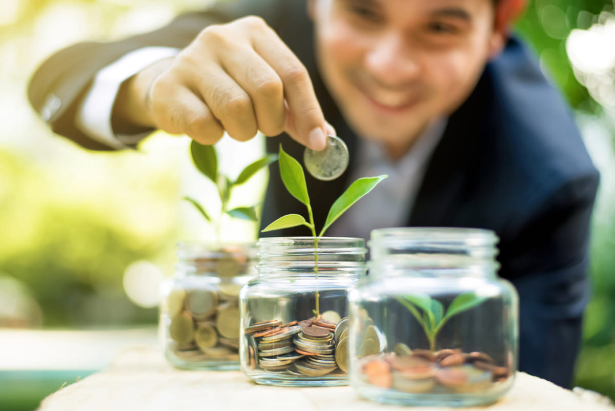 Man putting coins in jars with growing plants, build wealth through passive real estate concept