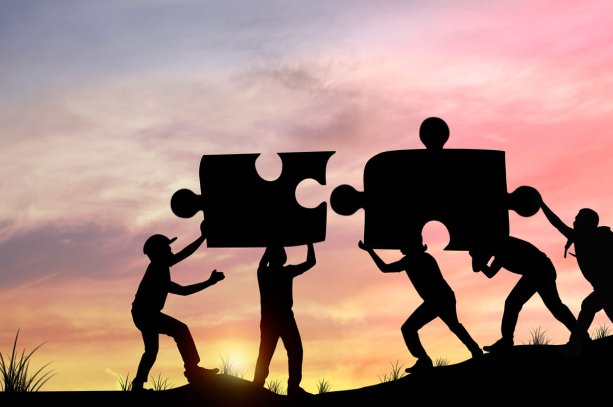 Silhouette of people helping each other put puzzle pieces together