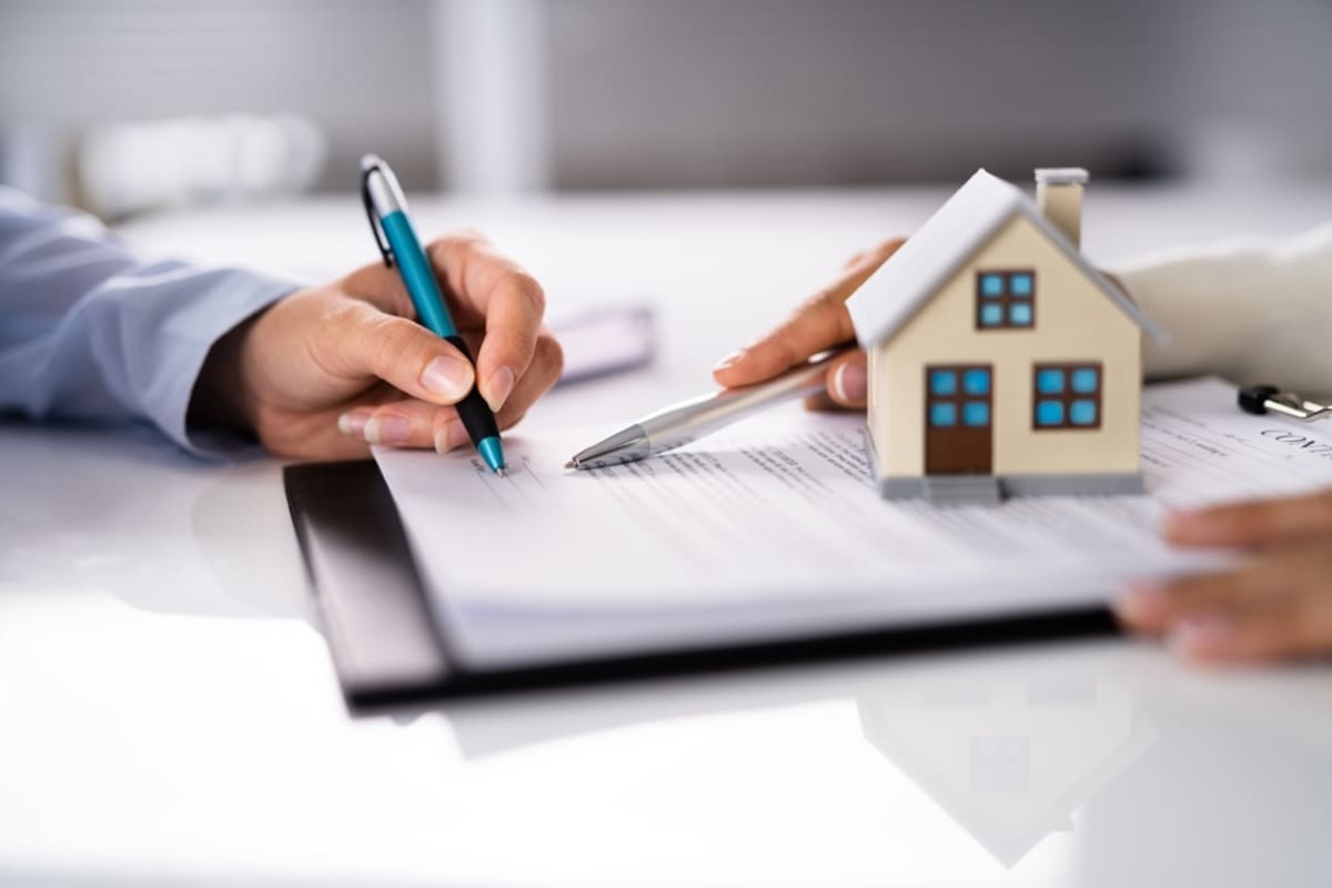 Someone directing someone where to sign on a document next to a model home
