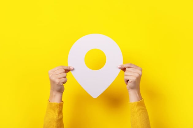 Someone holding a white map pin in front of a yellow background