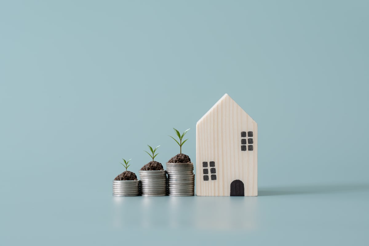 Stacked coins with plants on top next ot a model of a home