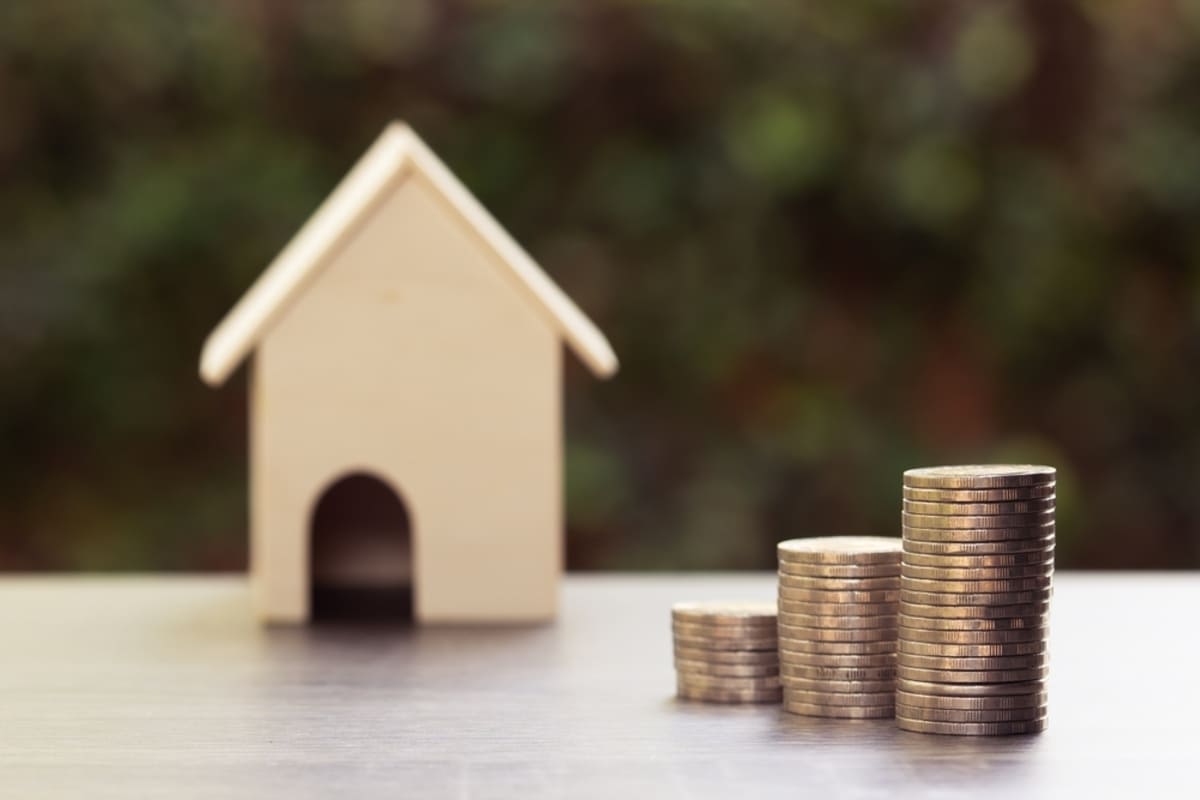 Stacks of coins next to a model house, passively invest real estate concept