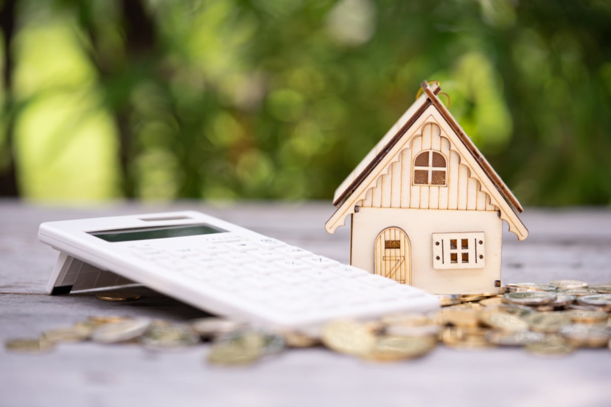 Calculator with stack of coins and wooden house icon as background