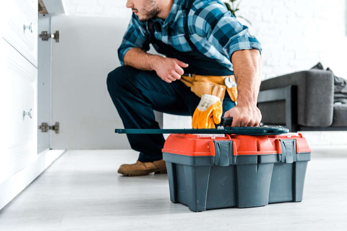 Cropped view of bearded handyman sitting and holding toolbox (R) (S)