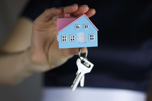 Person holding a set of keys on a keychain with a small house model