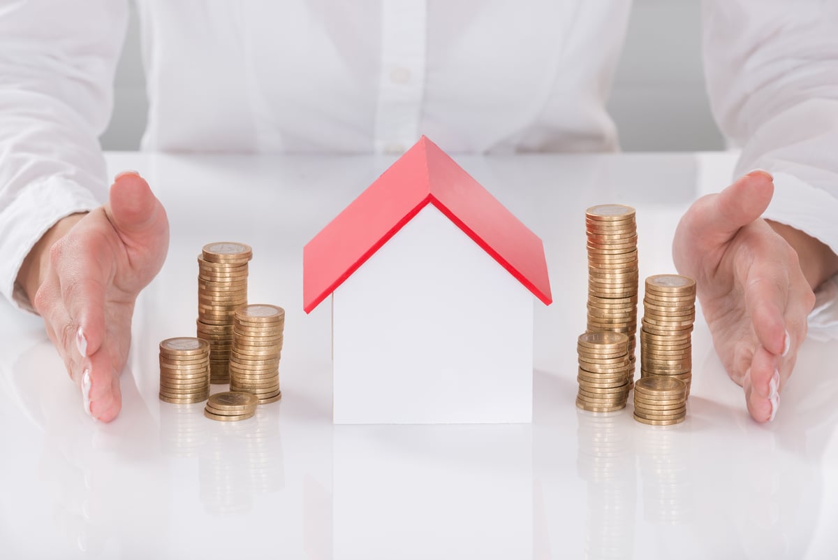 Hands Protecting House Model And Stacked Coins