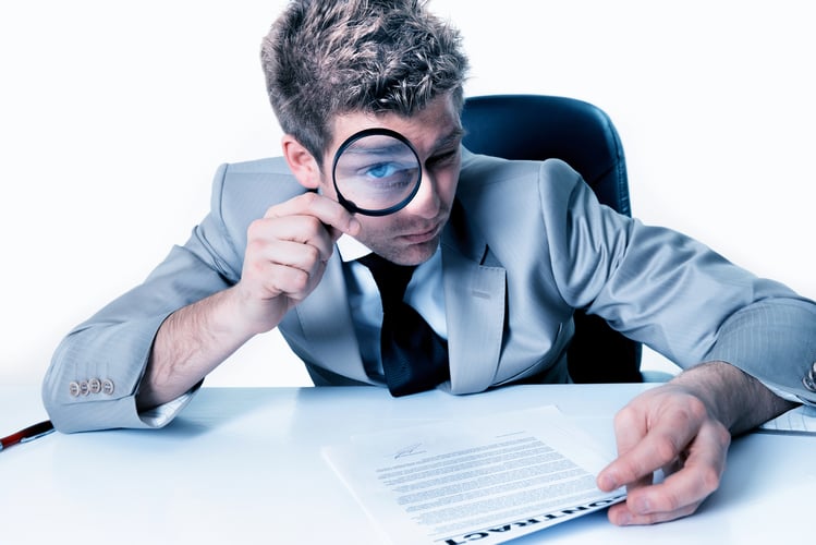 Man in a suit looking through a magnifying glass reading a document