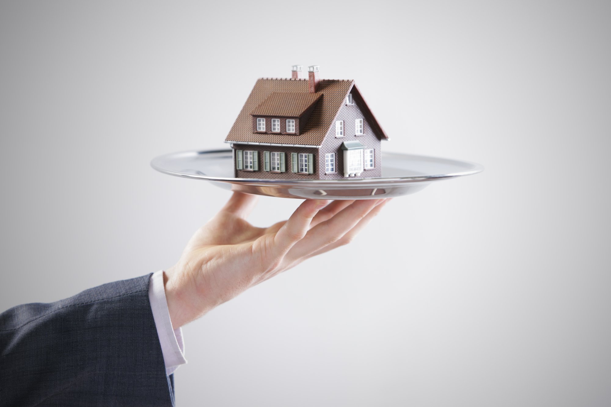 A hand holds a model house on a platter, Detroit property for sale concept. 