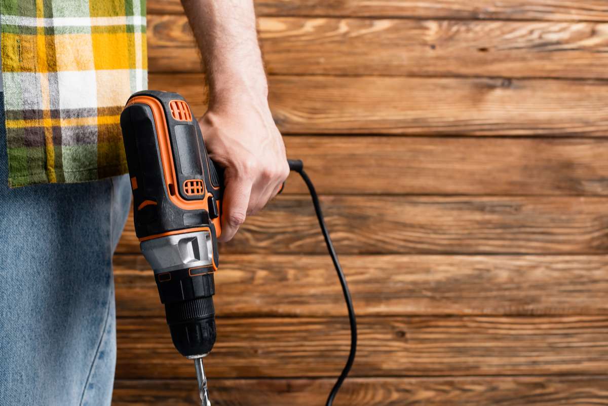 Partial view of builder with electric drill near wooden wall, labor day concept (R) (S)