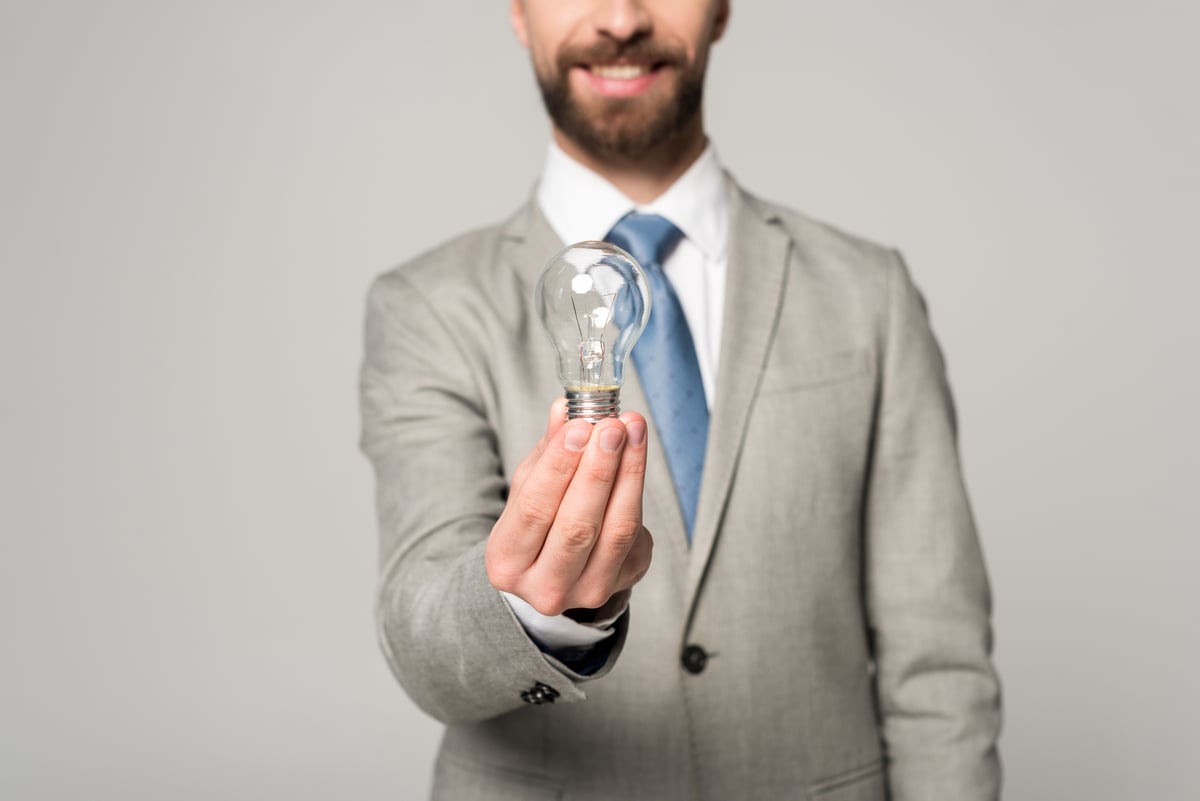 Partial view of smiling businessman holding light bulb isolated on grey