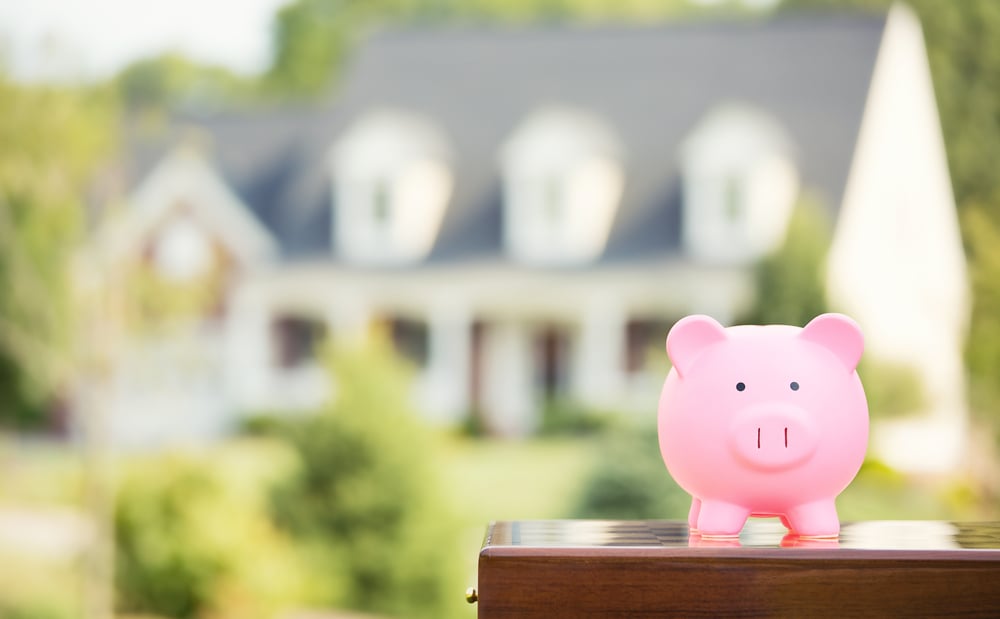 Piggy bank in front of a house, building a financial cushion to invest in Detroit real estate market concept. 