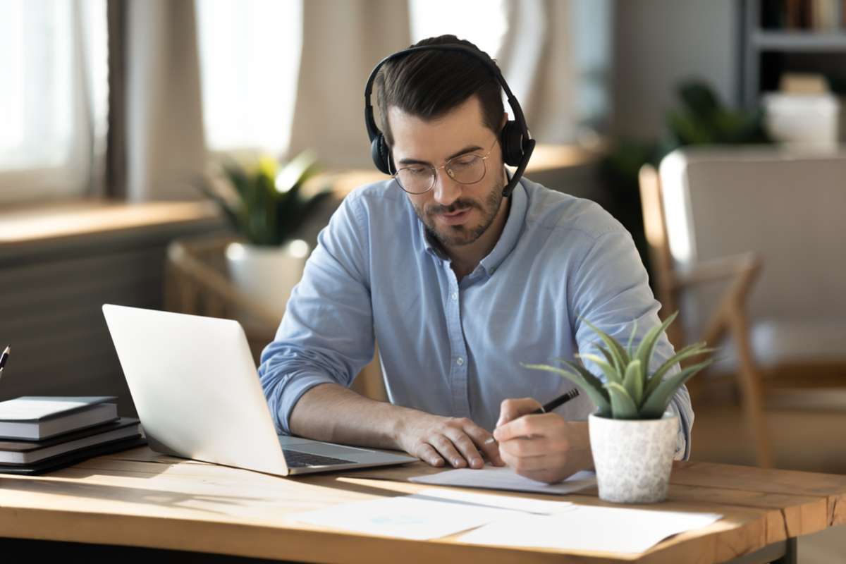 A businessman with headphones and a laptop watches online real estate investing courses