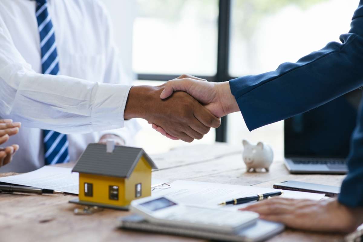 A handshake near a model house and piggy bank, Detroit rental property management