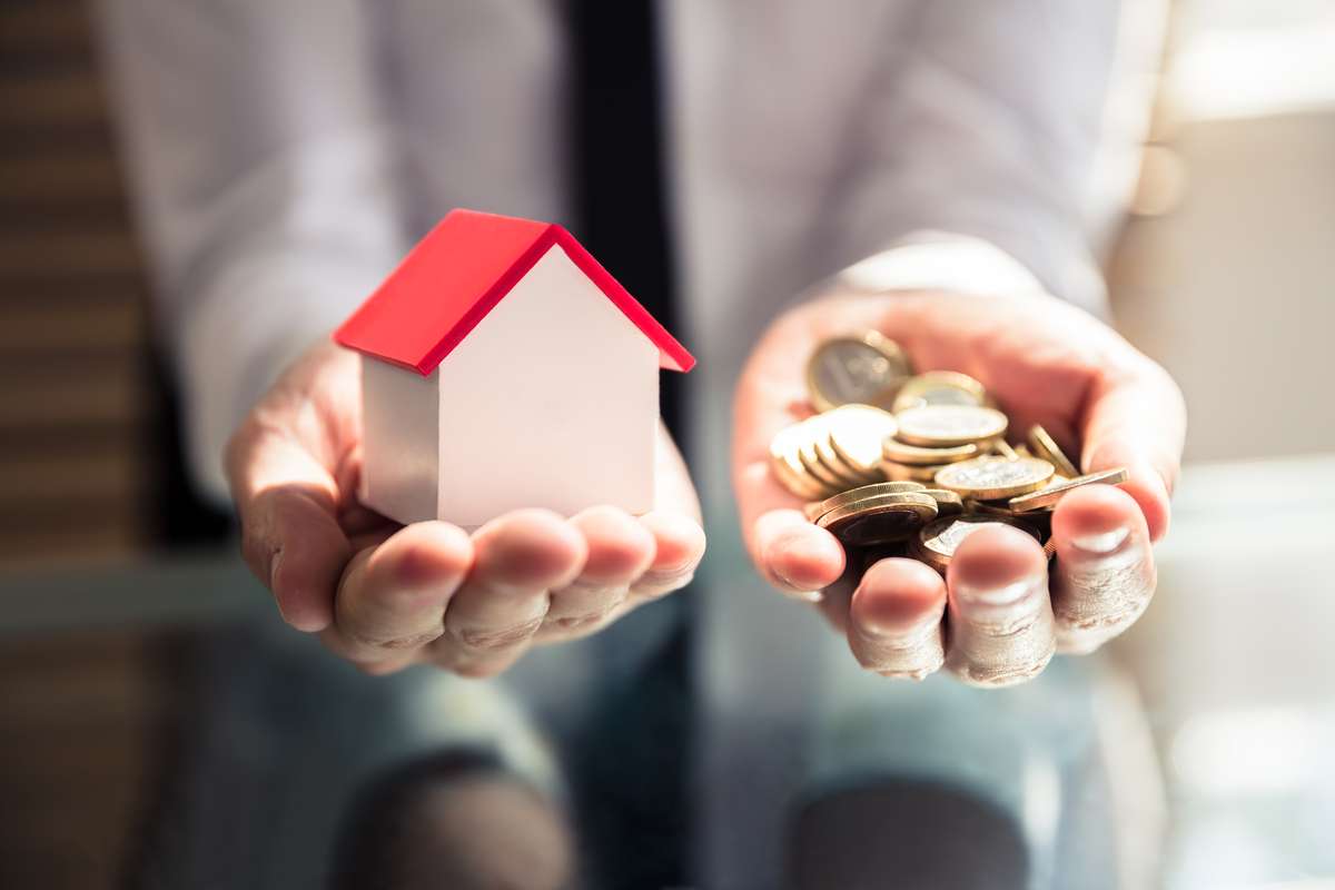 Close-up Of A Businesspersons Hand Holding House Model And Golden Coins