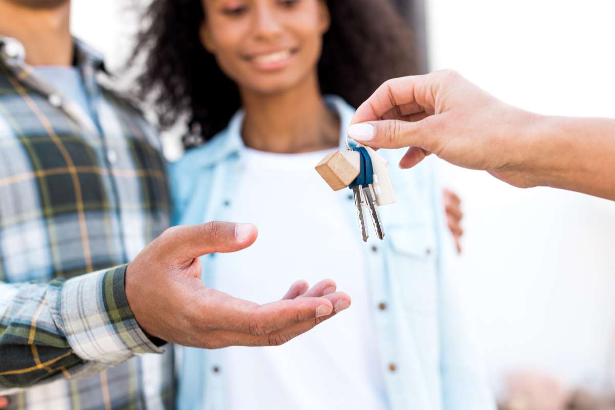 Cropped view of african american woman giving key of new house to happy couple