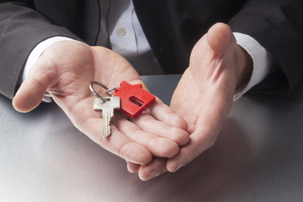 Hands holding a red house key, Detroit property management companies concept