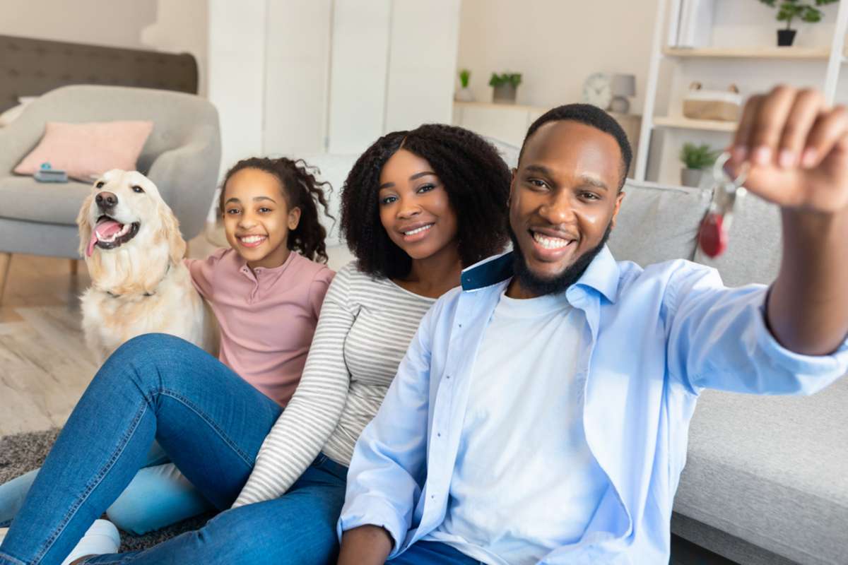 Happy African American family of three people and a dog holding and showing keys of their new apartment house