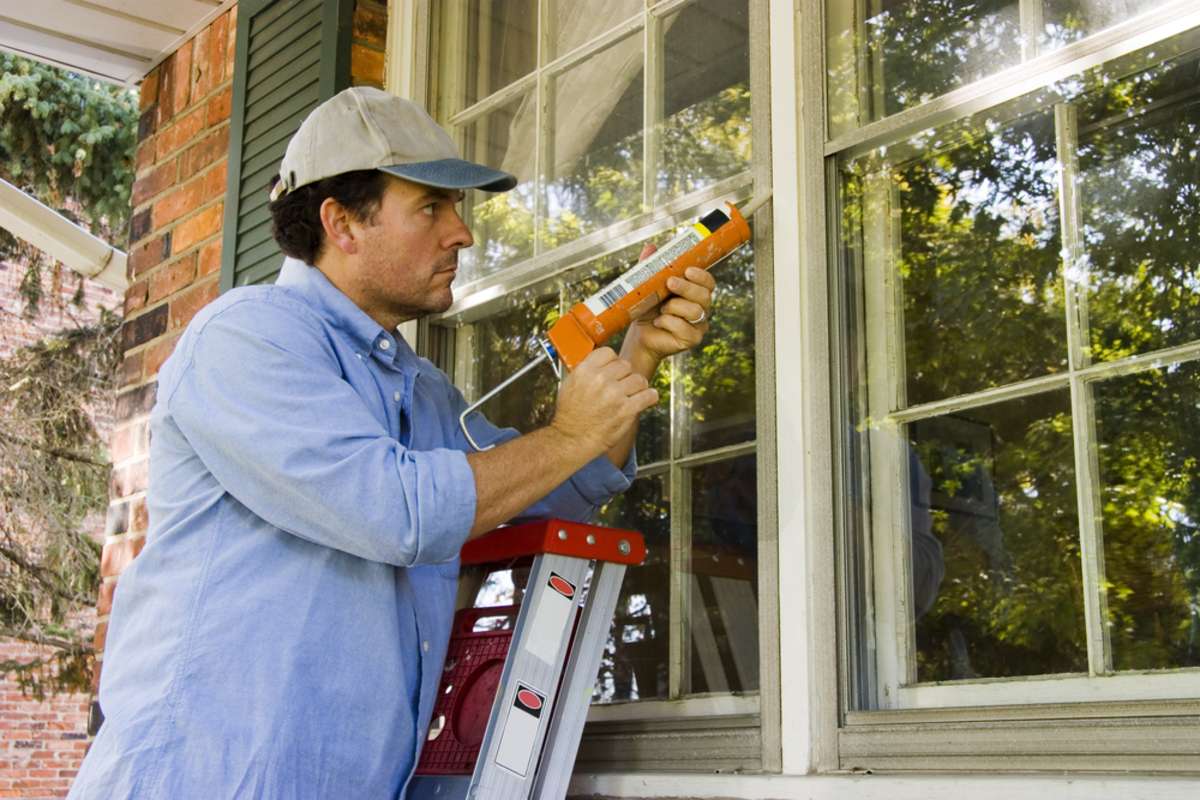 Man caulking windows, using a property management system for home maintenance concept