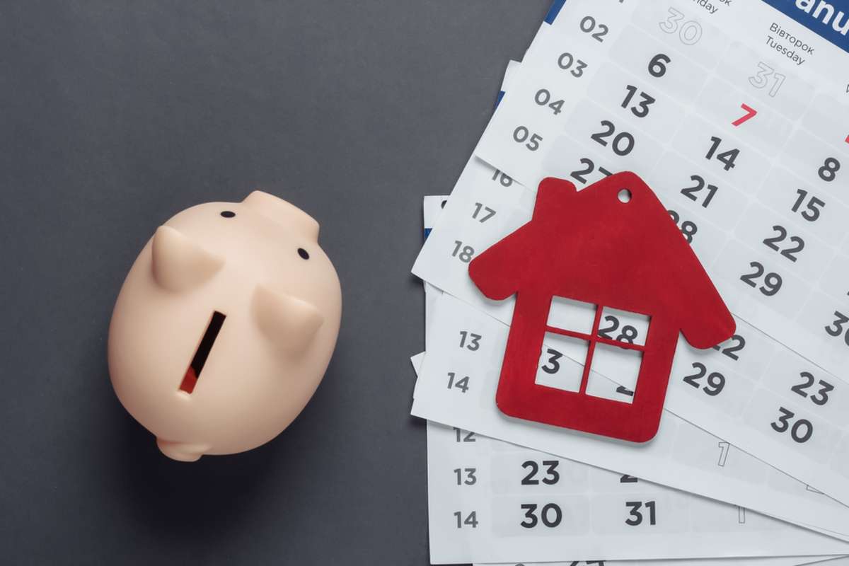 Piggy bank, house figurine with monthly calendar on gray background