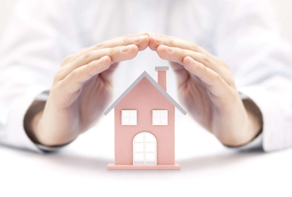 Property insurance. House miniature covered by hands