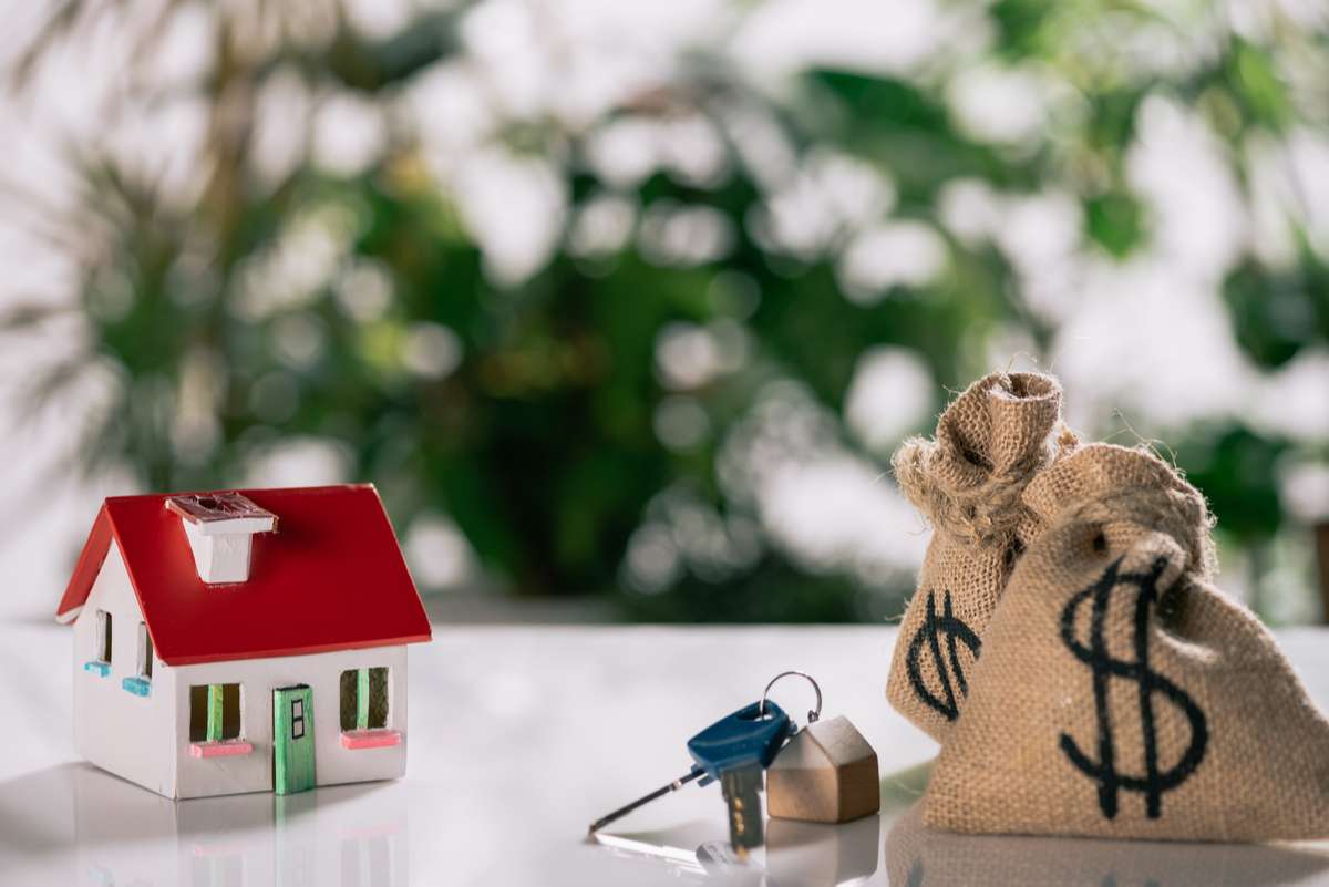Selective focus of keys, house model and moneybags with dollar signs on white desk, mortgage concept