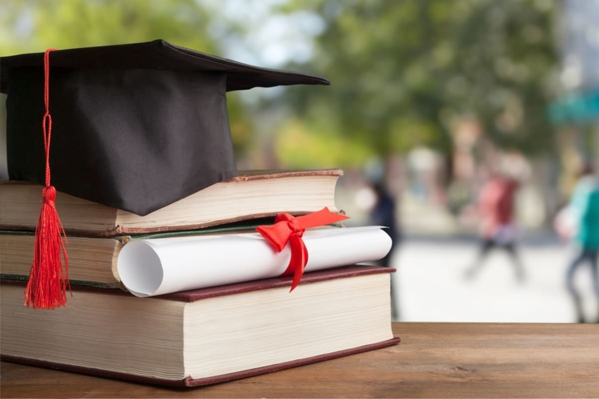 A graduation cap and a diploma on top of textbooks