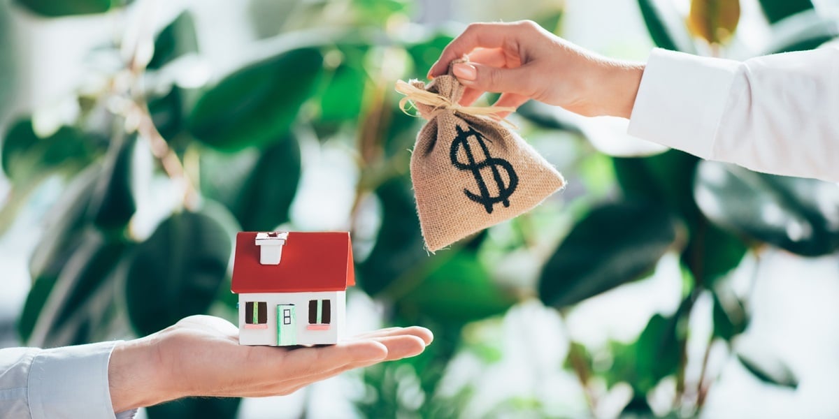 Someone holding a small bag labeled with a dollar sign and someone holding a small house