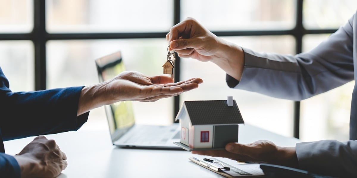 Someone holding a small house and handing a man house keys