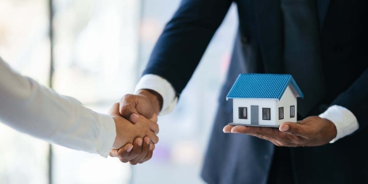 Two professionals shaking hands and holding a small model of a house