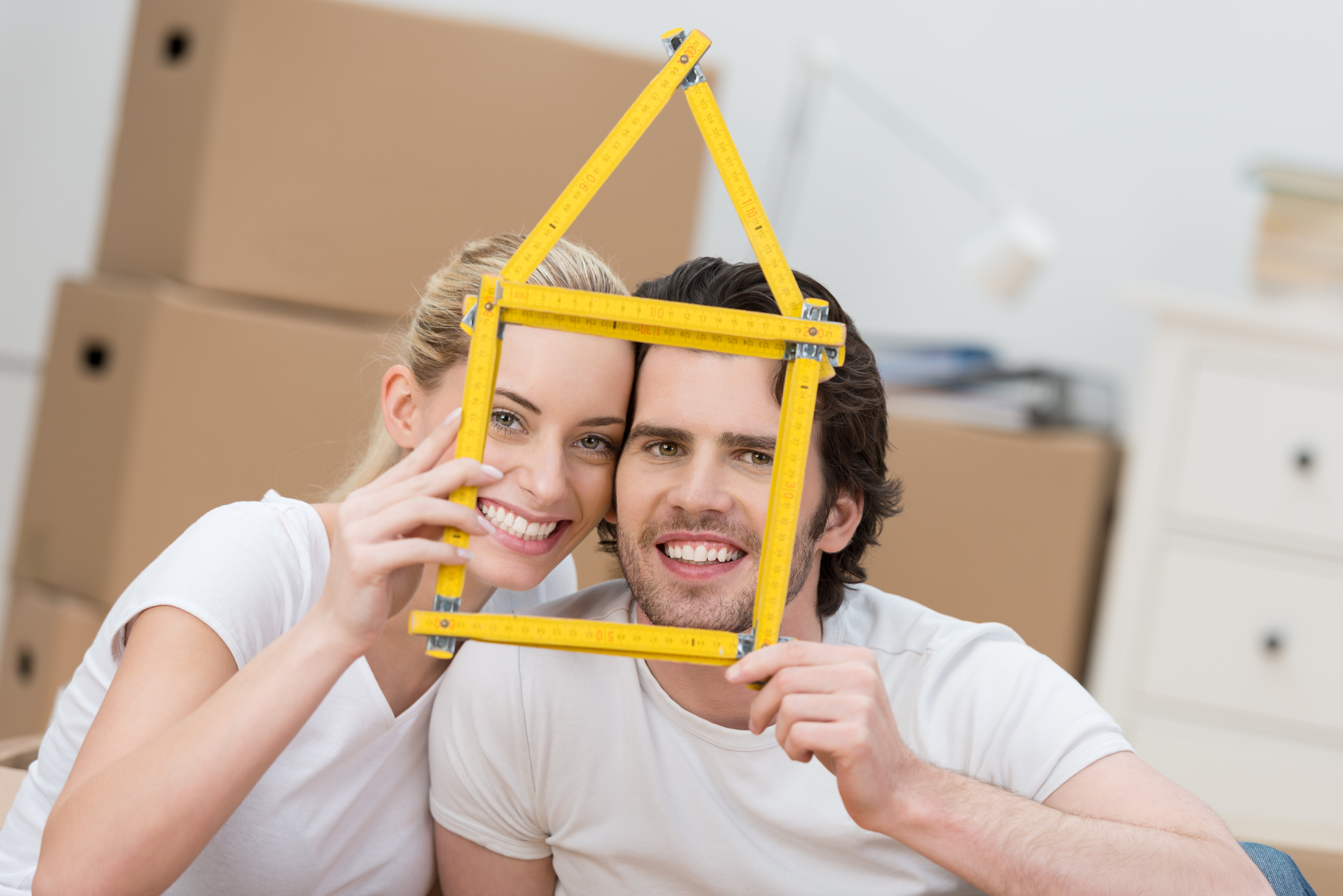 Young couple dreaming of their new home grinning as they hold up a builders ruler shaped as the frame of a house