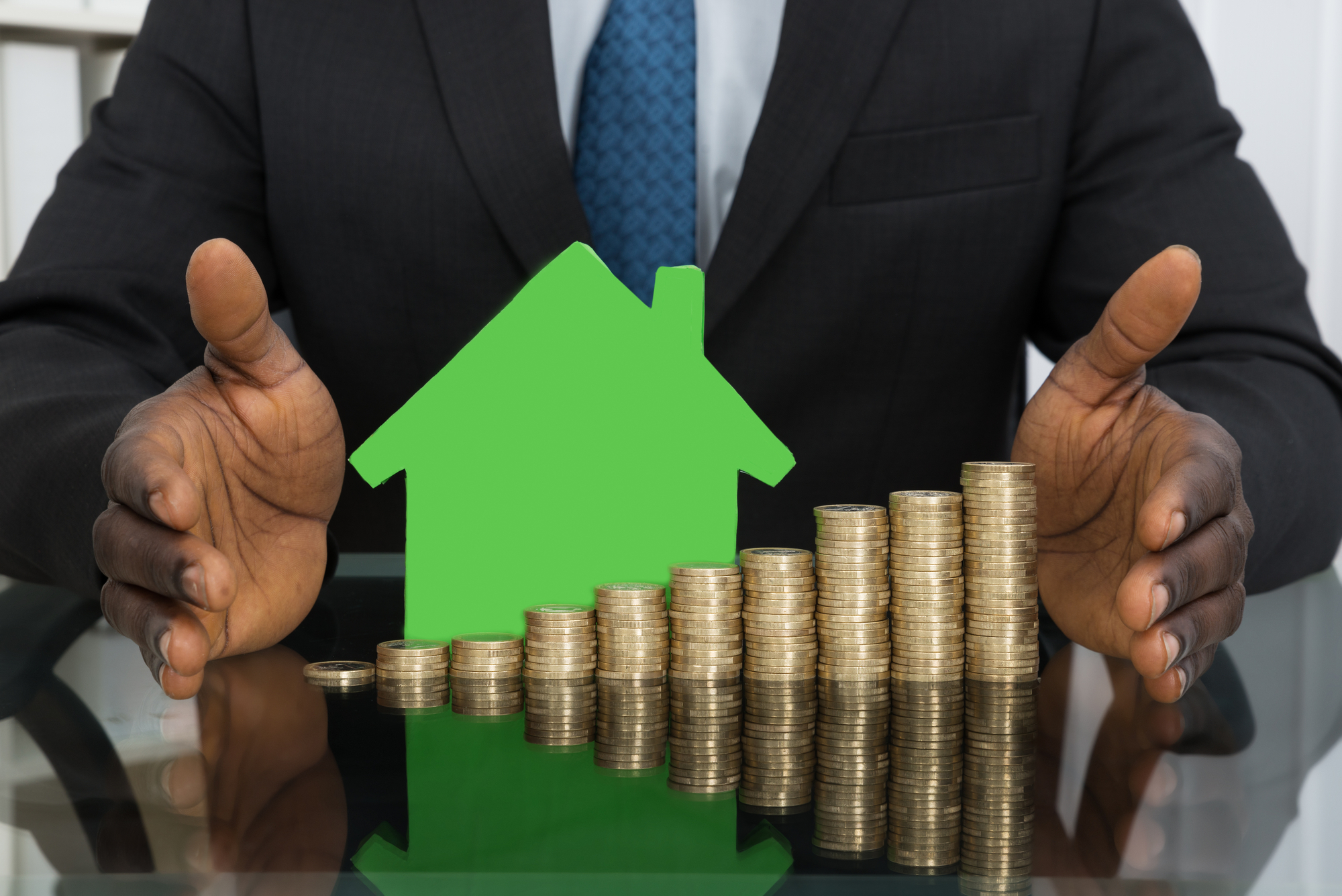 A green miniature house behind a stack of coins