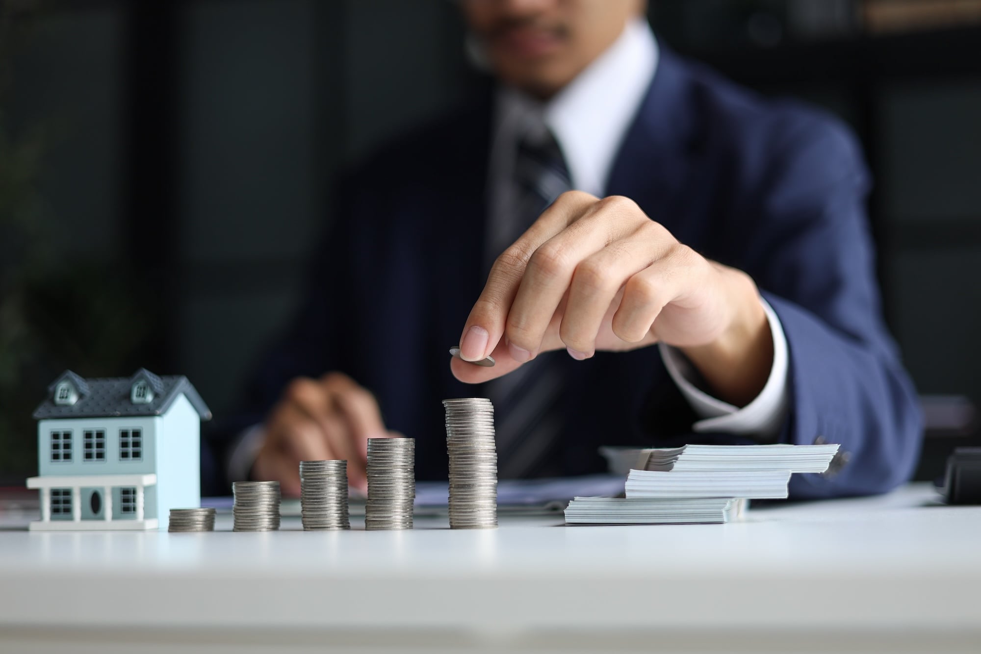 Man stacking coins near model house on desk