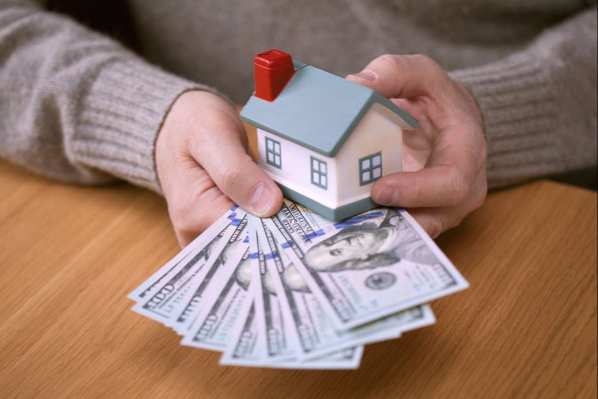 Hands holding a miniature house with cash