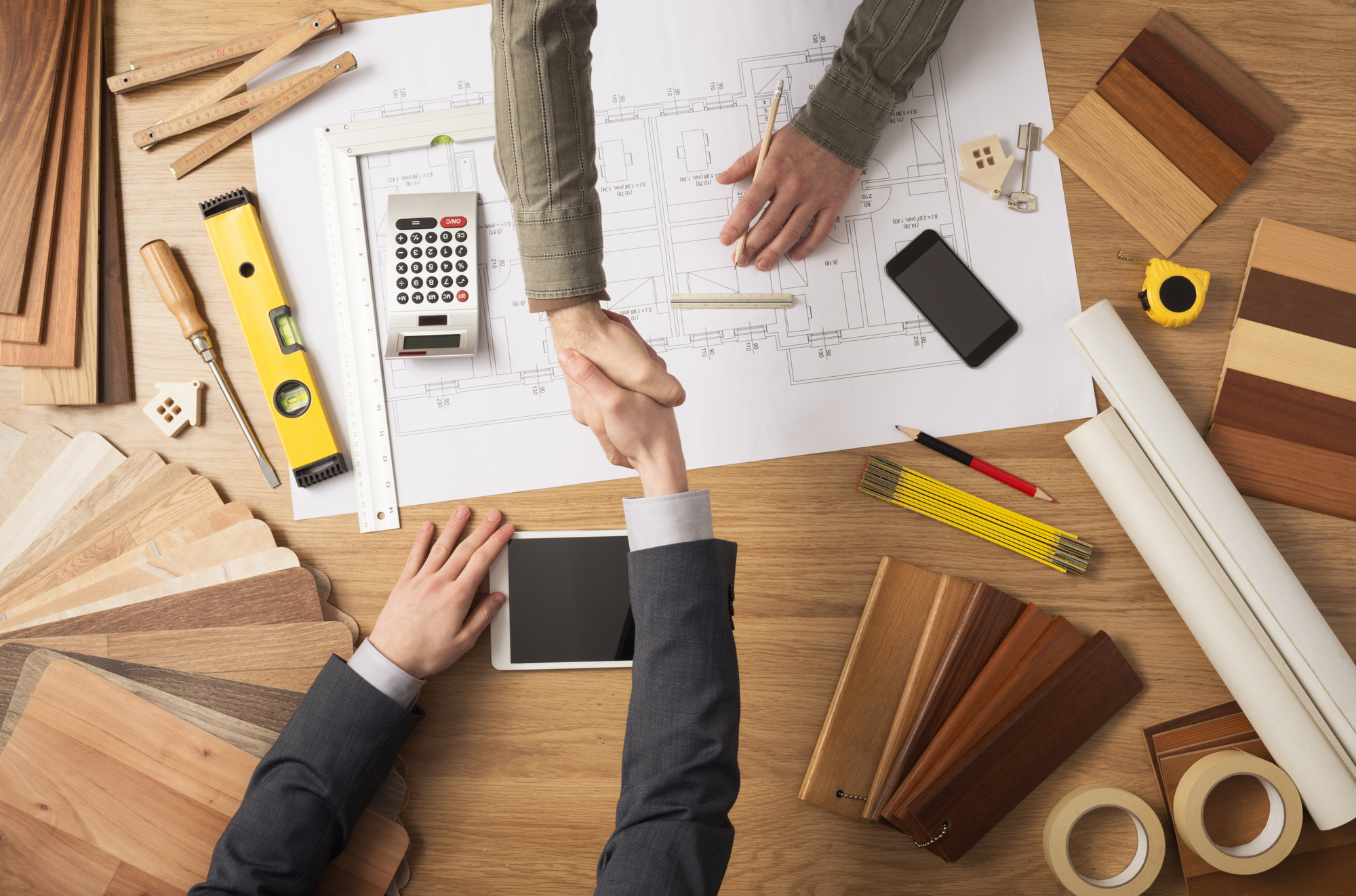 Businessmen shaking hands with a house plan in the background