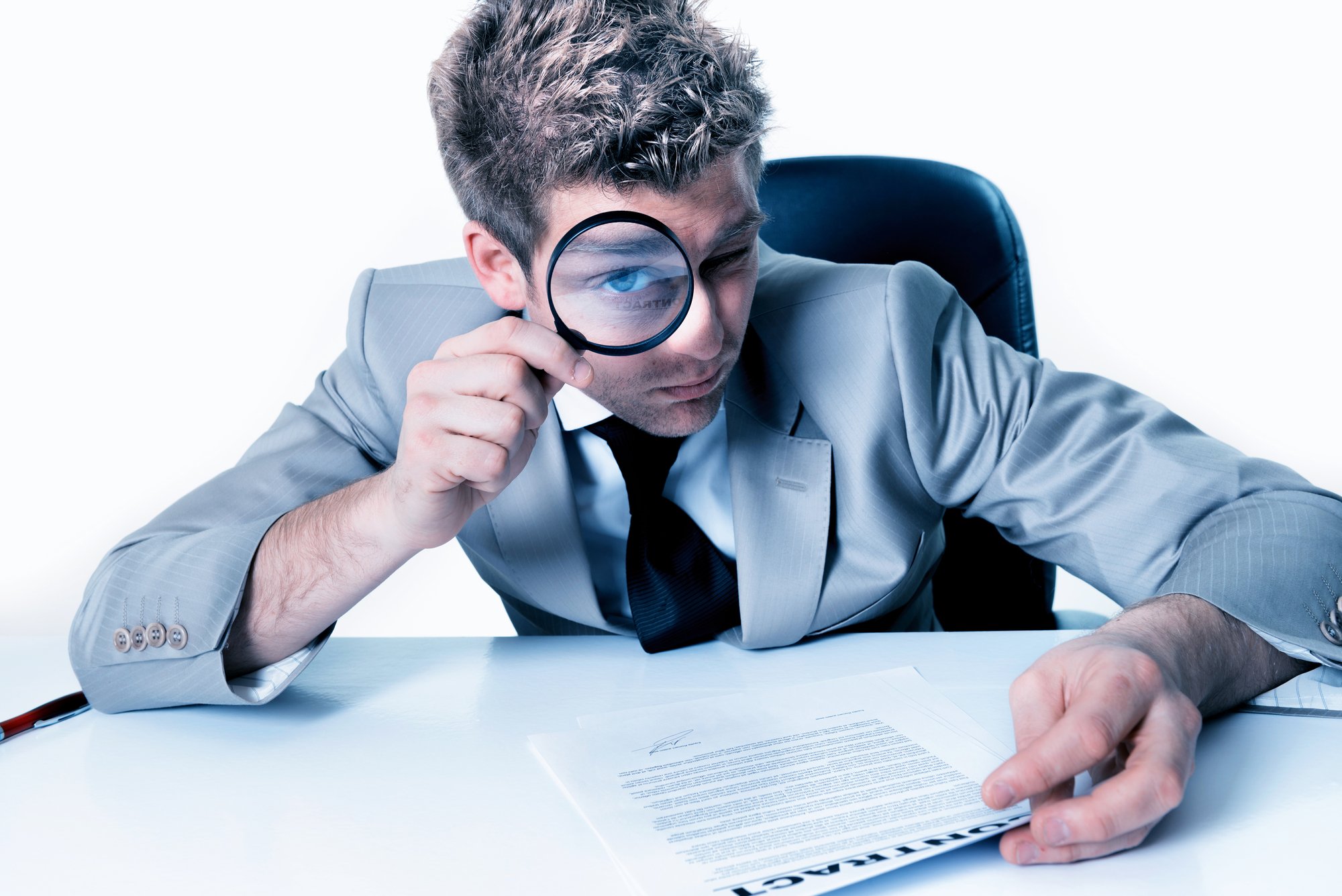 Man in a suit looking through a magnifying glass reading a document