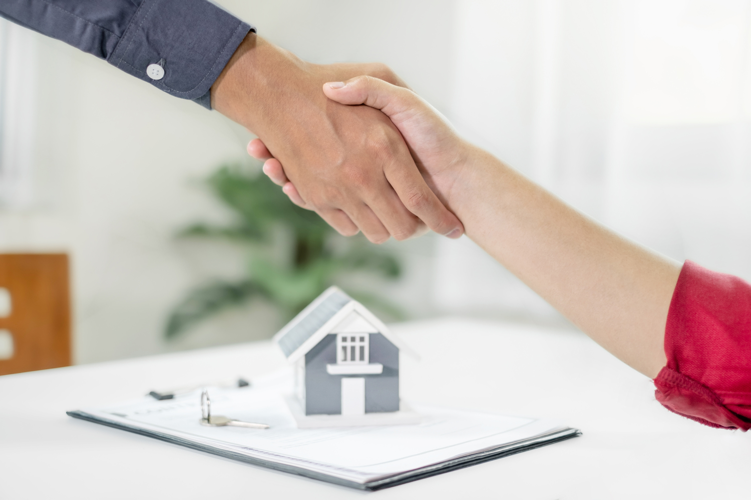 Two people shaking hands next to a small house and a contract Two people shaking hands next to a small house and a contract