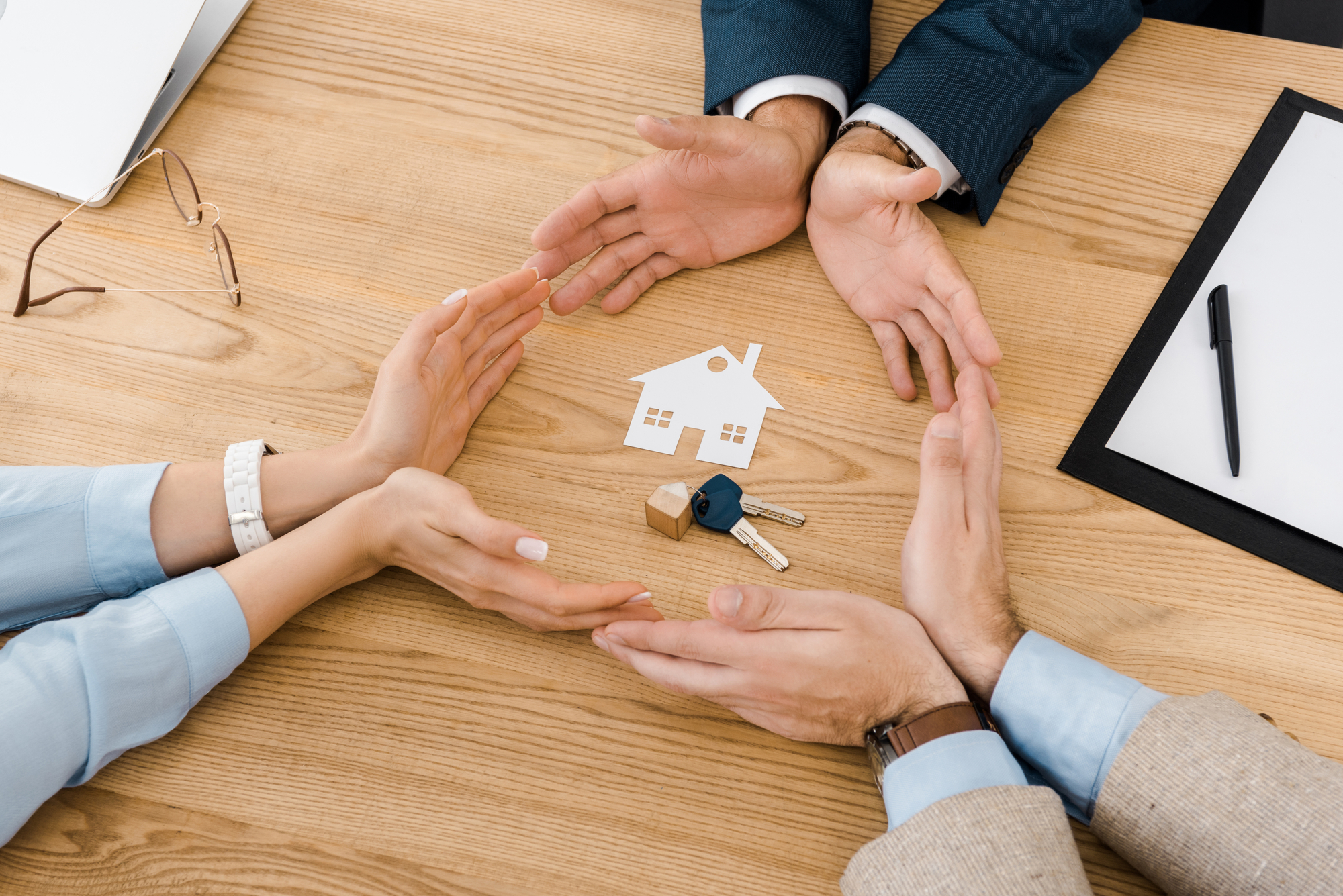 Businesspeople with their hands together forming a circle with a house cutout and keys in the middle