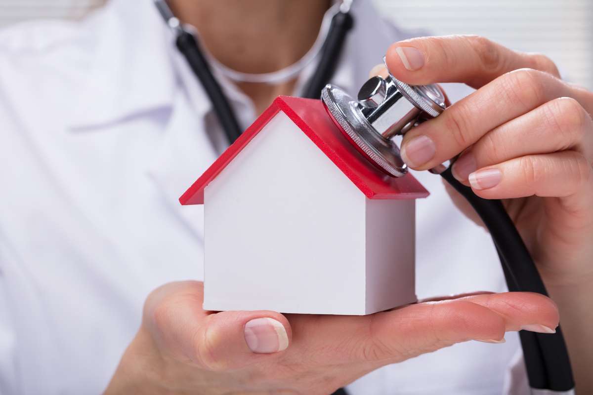 A person using a stethoscope on a miniature house
