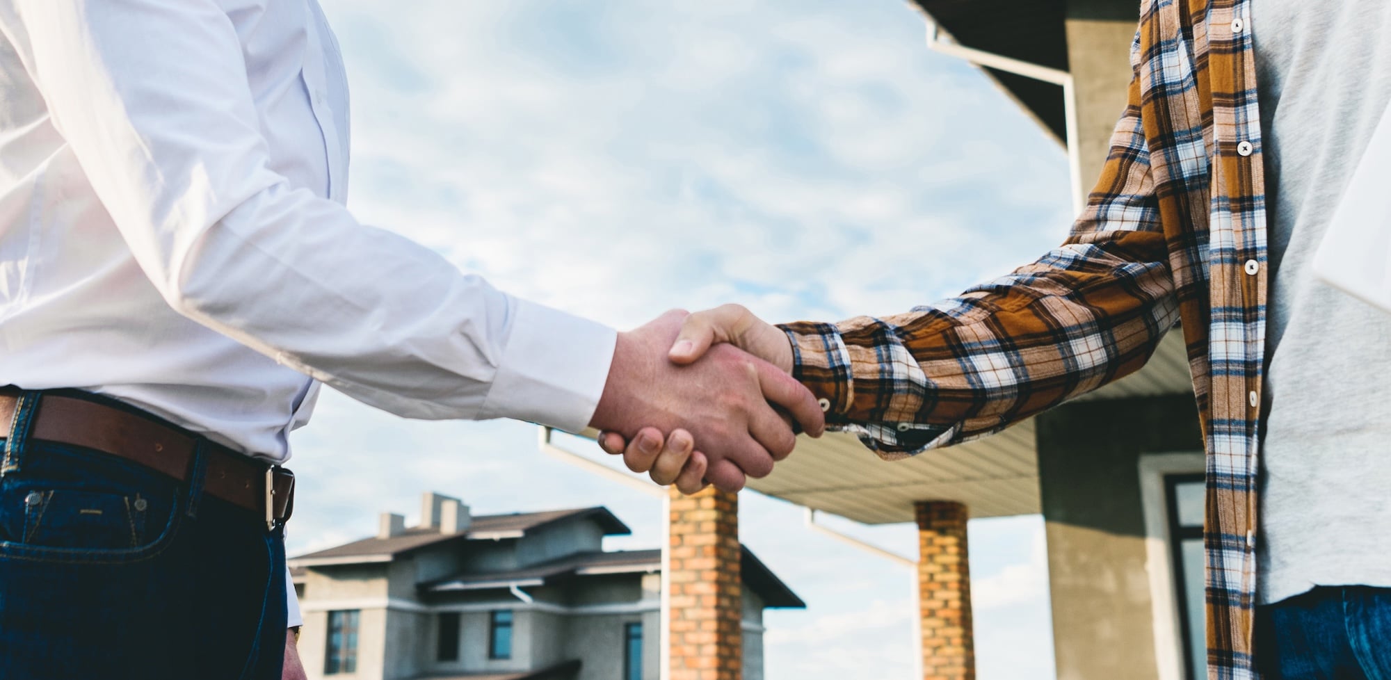 Landlord and tenant shaking hands in front of a property
